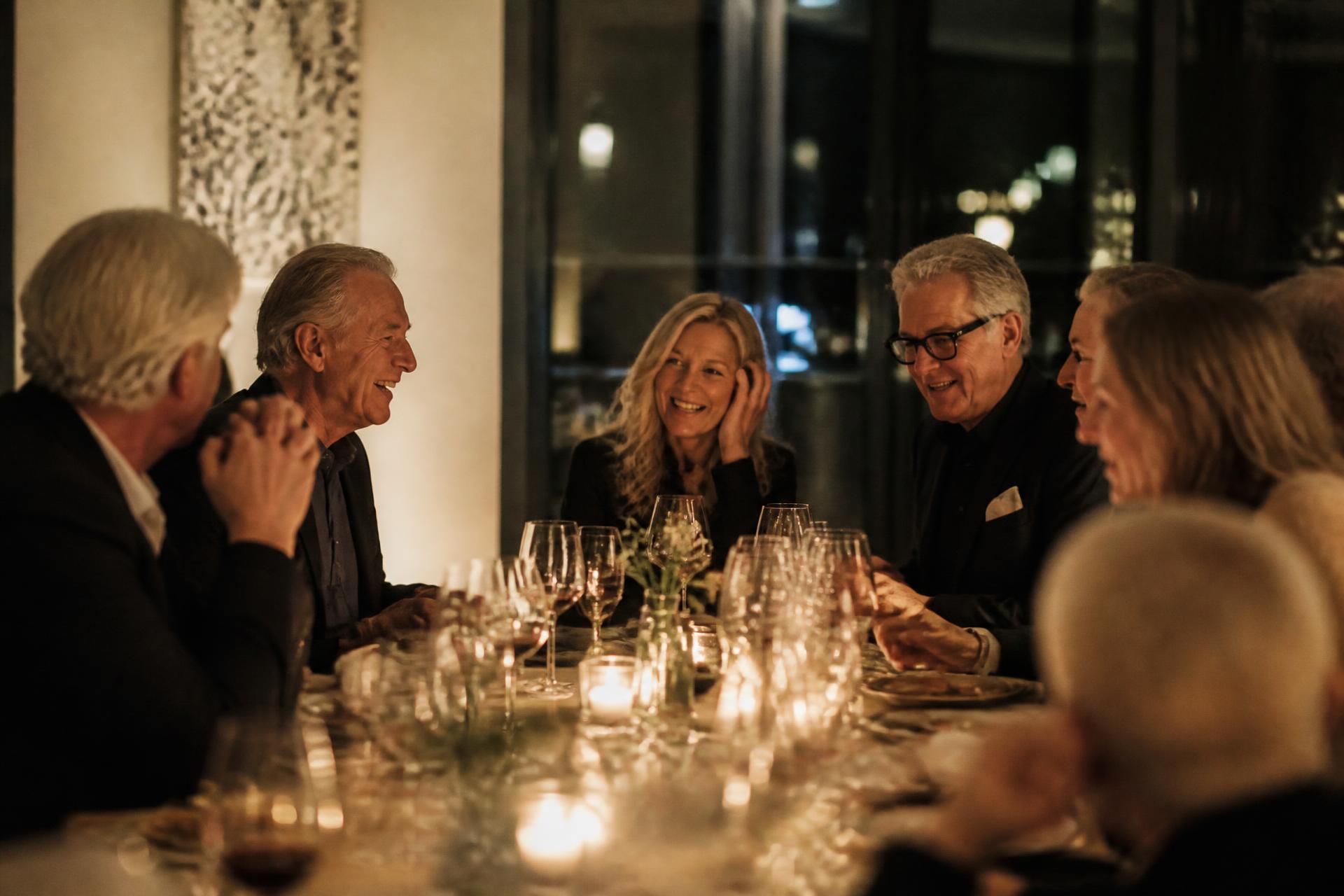 Friends laughing around a candlelit dinner table in a modern restaurant